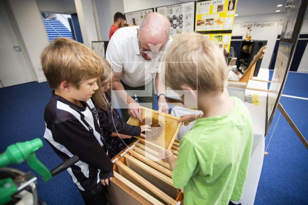 Picture by Sophie Rabey.  21-09-24.   Guernsey Beekeepers show at Beau Sejour with a range of classes for honey, wax, candles, cooking and photography.
Beekeeper Clive Weldon showing siblings L-R Lorna Beatty (6), Ryan Beatty (6) and Michael Beatty (8) how a hive functions.