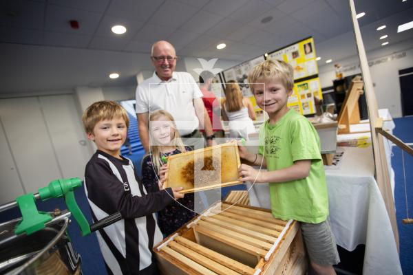 Picture by Sophie Rabey.  21-09-24.   Guernsey Beekeepers show at Beau Sejour with a range of classes for honey, wax, candles, cooking and photography.
Beekeeper Clive Weldon showing siblings L-R Lorna Beatty (6), Ryan Beatty (6) and Michael Beatty (8) how a hive functions.