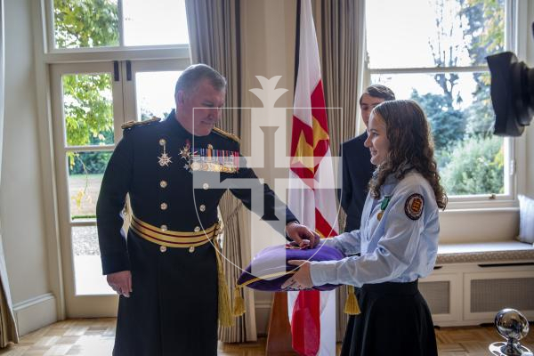 Picture by Luke Le Prevost. 02-12-23.
Investiture of Lucy Beere who received her MBE, by the Lieutenent Governor at Government House, for her sporting achievements. L-R Lt Governor collects the medal from Lt Governor cadet Carmen Walsh (16) with another Lt Governor cadet Jean-Pierre Lenormand (16) stood behind