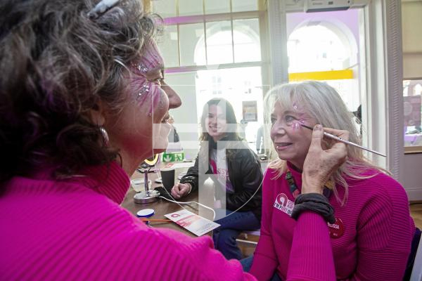 Picture by Peter Frankland. 24-02-24 Guernsey Arts Day in Market Square. Jennifer Strachan applies facepaint to Melissa Mock while Grace Stevens looks on.