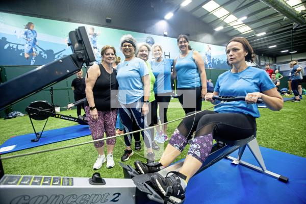 Picture by Peter Frankland. 25-02-24 MS Rowathon at Aztech Centre. Alex Herschel on the machine while her team mates from ' Ever the Optimists' look on.