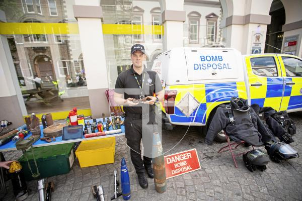 Picture by Sophie Rabey.  22-06-24.  Guernsey Bailiwick Law Enforcement held a Police recruitment drive in Market Square, showing off the different types of jobs you could work in within the police force.
PC James De La Mare with the bomb disposal stand, holding a piece of a ordance that was left after the detonation of an unexploded bomb in Lihou.