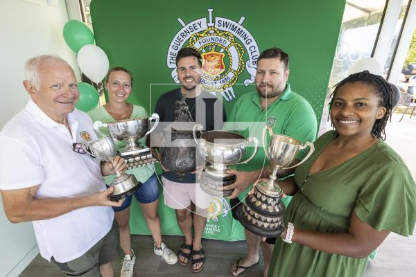 Picture by Peter Frankland. 23-08-26 The Guernsey Swimming Club celebrated their 140th anniversary today with a BBQ at La Vallette. L-R - Chris Butt, (President) holding the James Newbury Cup dating back to 1888, Heather Jackson, (coach) holding one of the States' cups which was paid for by the States of Guernsey at the time, Kevin Penney, (Vice President) holding the Urn presented to 400m free champion and dating back to 1888, Matt Butt, (Head coach) holding another of the States cups and Chido Chibaya, (Treasurer) holding the Curr Cup for youngest swimmer swimming 10m unaided and dating back to 1948.